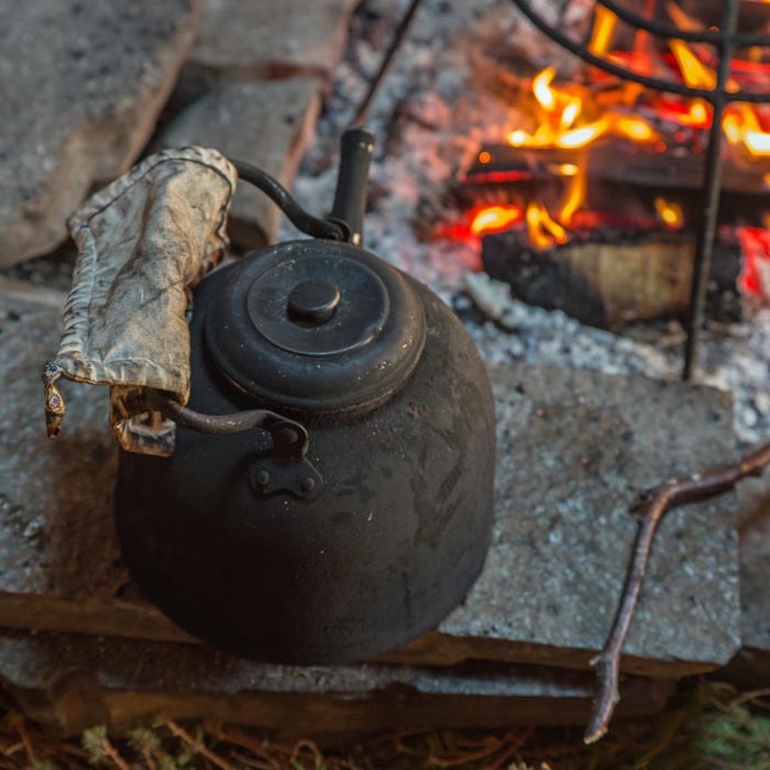An iron kettle sits beside a campfire