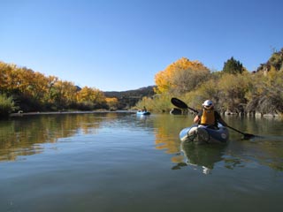 kayak on calm river with golden-leaved trees behind and mountain in the distance